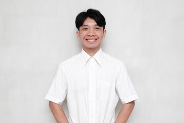 Asian young man wearing white shirt smiling cheerfully against isolated background