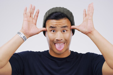 Funny face, portrait and Asian man in studio with tongue out, hands and silly on white background....