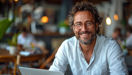 Fototapeta premium A happy businessman sitting at his desk in an office, smiling and looking into the camera with glasses on. He is wearing white shirt Smiling Businessman in Modern Office with Laptop - 4K HD Wallpaper