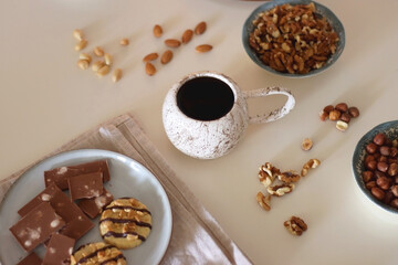 Cup of tea or coffee, cookies, macaroons, chocolate, various nuts and cocoa powder on white background. Selective focus.