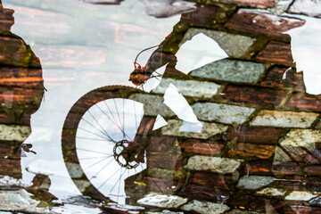 Reflection of person and bicycle in a puddle of rainwater in the river.