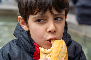 Boy biting traditional squid sandwich outdoors on Major Square at Madrid downtown in San Isidro