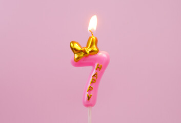 Burning pink birthday candle with golden bow and word happy on pink background, number 7.