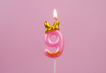 Burning pink birthday candle with golden bow and word happy on pink background, number 9.