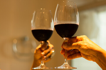 Hand holding a glass goblet with red wine next to a mirror.