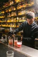 Bartender makes delicious cocktails in vintage night pub with wide selection of alcohol and drinks. Worker in uniform uses siphon to pour liquid