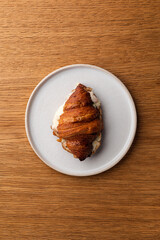 Stuffed Croissant Sandwich on a White Plate: Flaky Golden-Brown Croissant Filled with Scrambled Eggs, Ham, Cheese, and Fresh Vegetables, Served on a White Plate - Top View