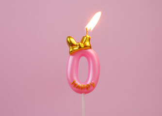 Burning pink birthday candle with golden bow and word happy on pink background, number 0.