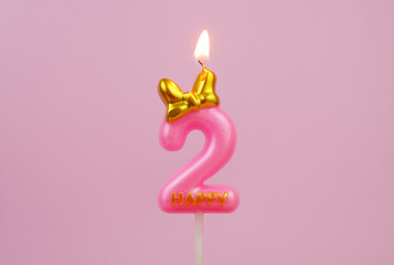 Burning pink birthday candle with golden bow and word happy on pink background, number 2.