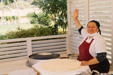 A woman preparing a large, thin piece of flatbread. She is working at an outdoor market stand,...