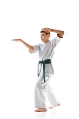 Focused martial arts student in white kimono and green belt prepares for fight, practicing isolated on white background. Concept of sport, martial arts, combat sport, healthy and active lifestyle