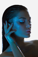 Woman with shimmering blue-tinted skin strikes a tranquil pose under cool lighting