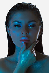 Womans face bathed in blue light, her skin adorned with sparkling glitter, exudes a contemplative...