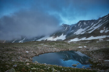 Tranquil mountain pond captures the fading light of dusk amidst alpine terrain