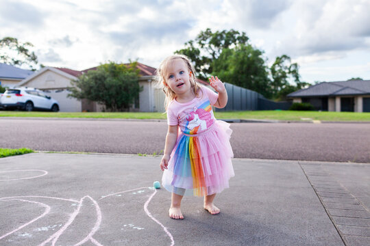 Happy little girl dancing on suburban driveway with chalk drawings