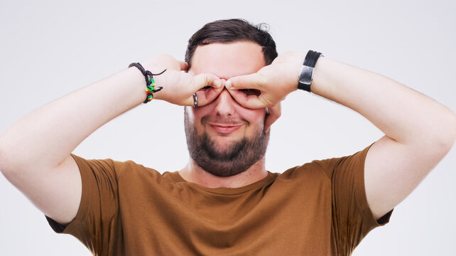 Studio, man and binoculars with hands for crazy comic, silly and goofy expression with smile. Face, male model and goggles sign, symbol and emoji for feedback or reaction by white background