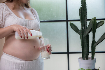 Pregnant woman holding a glass of milk on window background.