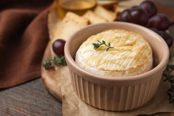 Tasty baked camembert in bowl on wooden table, closeup. Space for text