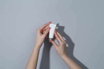 Woman holding tube of cream on grey background, closeup