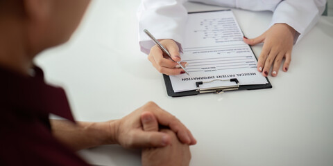 Doctor consulting male elderly patient filling medical form. Professional physician writing...