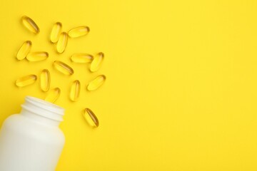 Softgel capsules and bottle on yellow background, top view. Space for text