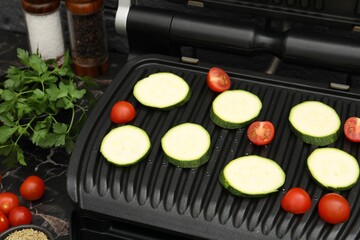 Electric grill with vegetables on black marble table, closeup