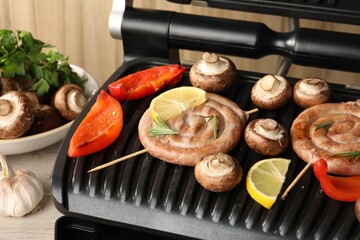 Electric grill with homemade sausages, mushrooms and bell pepper on table, closeup