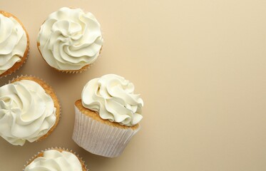 Tasty vanilla cupcakes with cream on beige background, top view. Space for text