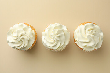 Tasty vanilla cupcakes with cream on beige background, top view