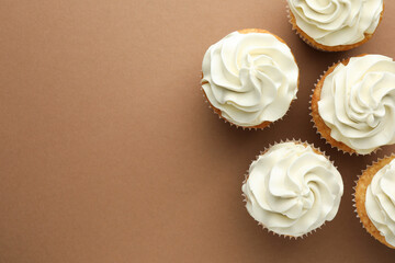 Tasty vanilla cupcakes with cream on dark beige background, top view. Space for text