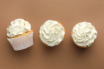 Tasty vanilla cupcakes with cream on dark beige background, top view