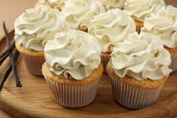 Tasty cupcakes with cream and vanilla pods on beige table, closeup