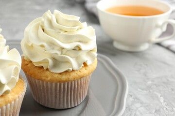 Tasty cupcakes with vanilla cream on grey table, closeup. Space for text