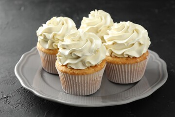 Tasty cupcakes with vanilla cream on black table, closeup