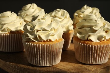 Tasty cupcakes with vanilla cream on wooden stand, closeup