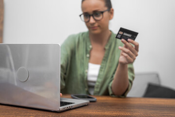 Credit card in hand, a woman with glasses takes care of online payments and shopping via her...