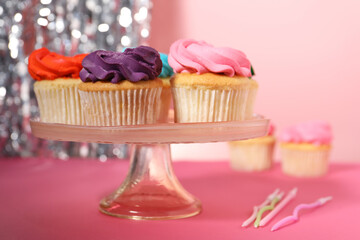 Delicious cupcakes with bright cream and candles on pink table