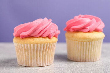 Delicious cupcakes with bright cream on gray table against violet background
