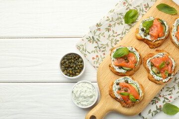 Tasty canapes with salmon, capers, cucumber and sauce on white wooden table, top view. Space for text