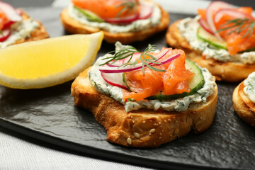 Tasty canapes with salmon, cucumber, radish and cream cheese on table, closeup