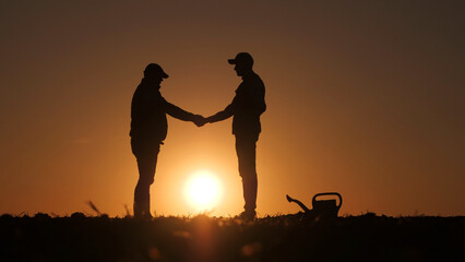 Silhouettes of two farmers shaking hands against the backdrop of the sun setting over a field