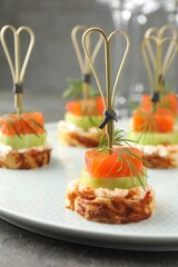 Tasty canapes with salmon, cucumber, bread and cream cheese on grey table, closeup