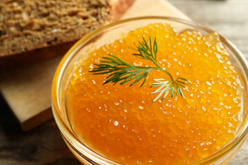 Fresh pike caviar in bowl and bread on wooden table, closeup