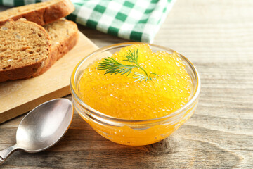 Fresh pike caviar in bowl and bread on wooden table, closeup