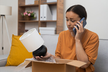 Stressed woman calls product delivery hotline on mobile phone with complaint about table lamp...