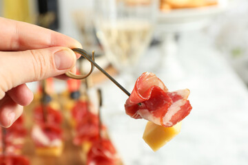 Woman holding tasty canape with cheese and prosciutto on table, closeup