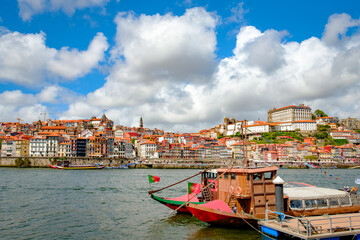 A photograph of the city of Porto intended for tourism on a sunny day. Concept: A city with traditional Portuguese architecture on the banks of the Douro River with two typical ships in foreground