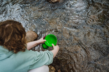 Woman kneels in water with green cup, enjoying leisurely recreation in nature
