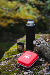 A first aid kit and a thermos rest on a rock in a grassy natural landscape
