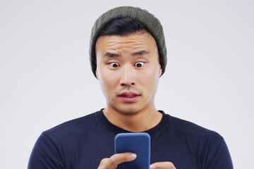 Asian man, surprise and phone on studio background with shock for reading article, social media and omg. Fraud, mobile and person with fear for online scam by grey backdrop for fake news and worry